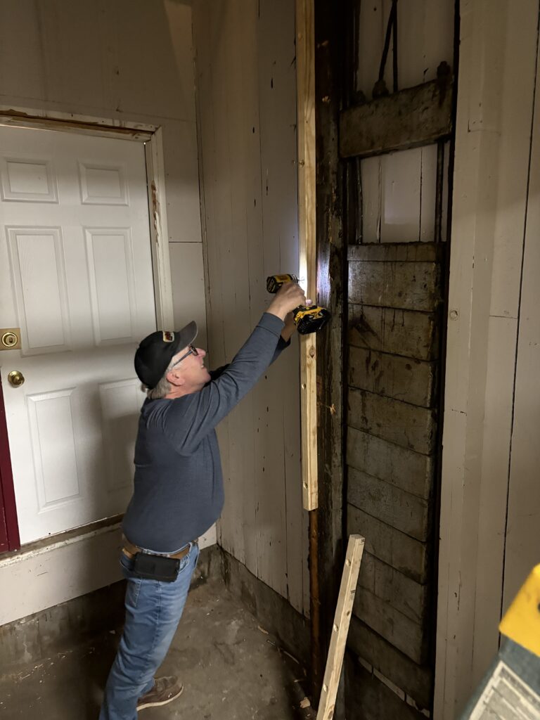 Person fixing wooden wall with power drill indoors.
